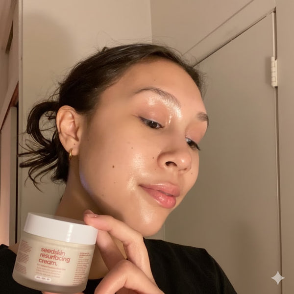 Person holding a jar of 'seedskid' resurfacing cream in front of their face.